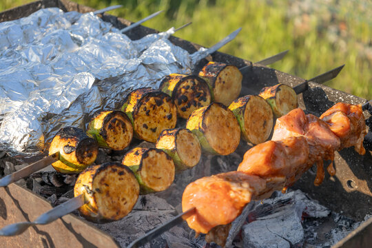 Delicious shish kebab and zucchini grilling on skewers over hot coals in a backyard grill. Meat and vegetables cooking outdoors during a sunny weekend picnic, preparing a tasty meal for family