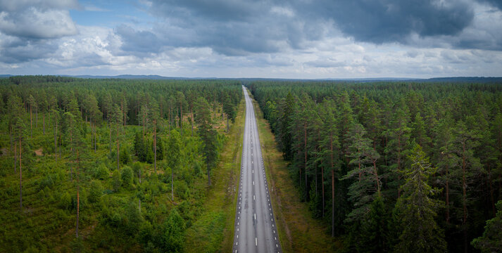 Top-down aerial view of a winding gravel road surrounded by dense green forest in the area around J&ouml;nk&ouml;ping, southern Sweden. The lush Scandinavian woodland creates a remote and untouched natural land