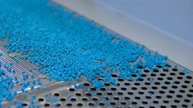 Plastic recycling machine: close up of moving blue propylene or polyethylene pellets, granules on a vibrating shale shaker, conveyor belt. Separation, sustainable, and waste reduction concept