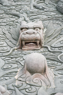 A detailed close-up of an ornate stone relief featuring a mythical beast amidst stylized waves and clouds. The sculpture showcases traditional Chinese craftsmanship and intricate textures in a garden