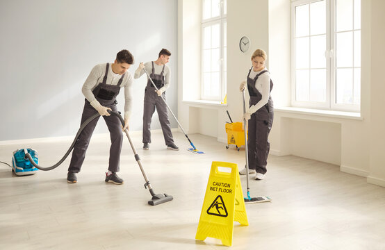 Cleaners janitors team cleaning mopping vacuuming. Crew maintains office with wet floor sign, ensuring spotless surfaces and workflow. Sanitation and housekeeping hygiene maintenance concept.