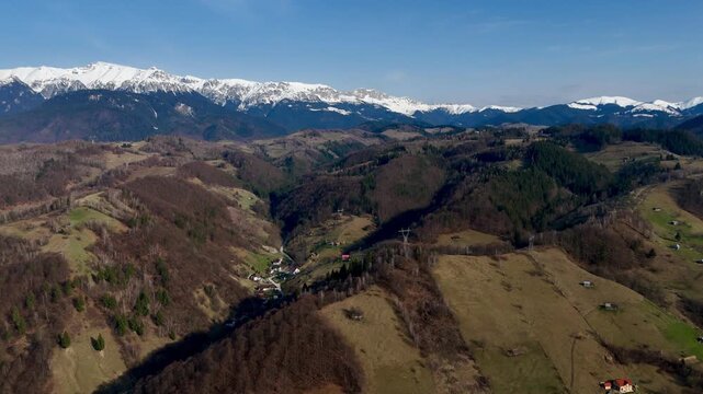 Aerial Panoramic View of Rolling Mountain Valleys and Snow-Capped Peaks Under a Clear Blue Sky