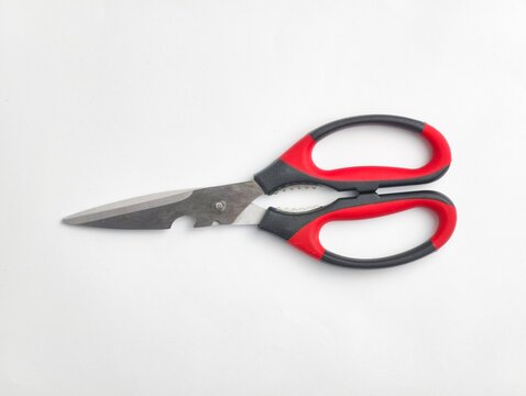 Top view of stainless steel kitchen shears featuring built-in bottle opener and red and black ergonomic handles, isolated on a white background.