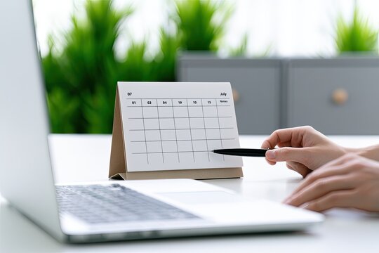 Person's hands pointing to a desk calendar next to a laptop