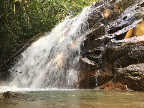 Beautiful tropical waterfall flowing over rugged rocks into a natural pool surrounded by lush rainforest, capturing a peaceful wilderness landscape and refreshing outdoor destination.