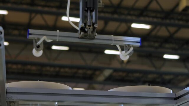 White polypropylene yogurt containers are moved by an automatic pick and place robotic arm manipulator with suction cups: plastic injection molding machine at exhibition, plant, factory - close up