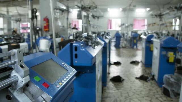 Camera moving smoothly along rows of automated knitting machines inside modern textile factory
