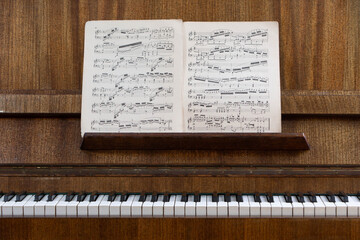 Vintage upright piano with classical sheet music on the music stand, showcasing timeless musical heritage, acoustic instrument, traditional composition and public domain music. © NataSao