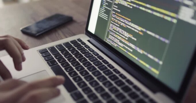 Close-up of hands typing on a laptop keyboard with programming code displayed on the screen, captured with a smooth orbiting camera movement.