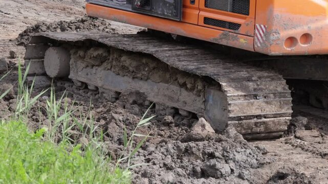 Weathered metal tracks and embedded soil reveal relentless work on unfinished ground. The gritty texture and mechanical mass convey raw power meeting rugged terrain