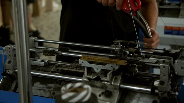 Industrial technician cleaning automated knitting machine with compressed air during routine maintenance in textile factory