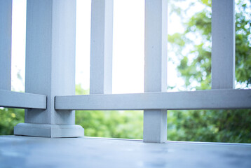 Fototapeta premium Close-up view of wooden balcony railing with vertical slats and horizontal support, overlooking green foliage and trees in a bright outdoor setting