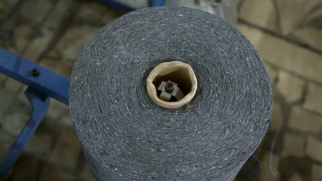 Large industrial yarn spool unwinds thread for automated knitting machine. Textile factory uses continuous material supply for efficient production.