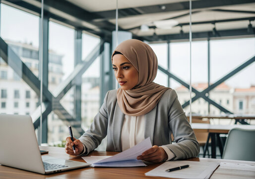 Happy muslim businesswoman in hijab at office workplace. Smiling Arabic woman working on laptop.