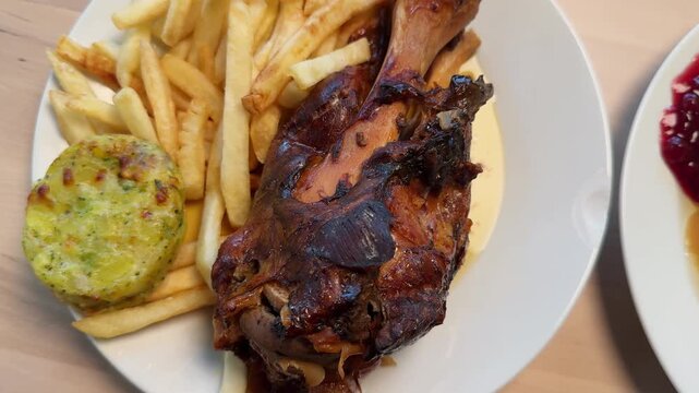Pork knuckle served with french fries on a plate. Hearty meat dish with crispy skin and traditional presentation. High quality 4k footage