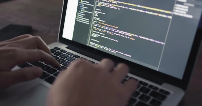 Programmer actively edits and modifies programming code while typing on a laptop keyboard.