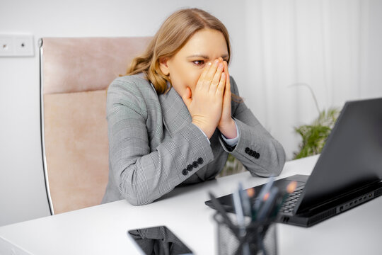 Woman business employee in grey blazer with hands on face at laptop desk Concept of professional burnout stress mental exhaustion