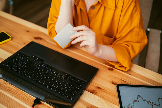 Close up of hands holding credit card near laptop and tablet with stock chart