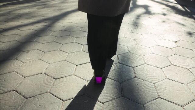 Back view of a woman's legs walking on a city street, wearing stylish heeled boots. High quality 4k footage