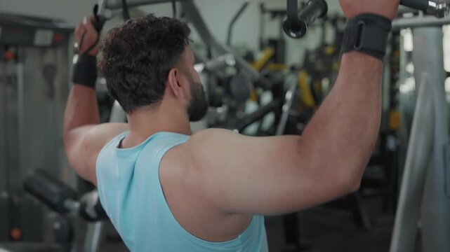 Indian Asian fit young man or male using a lat pulldown machine, performing resistance weight training exercise or workout targeting the back and shoulders in modern gym. Fitness, bodybuilding concept