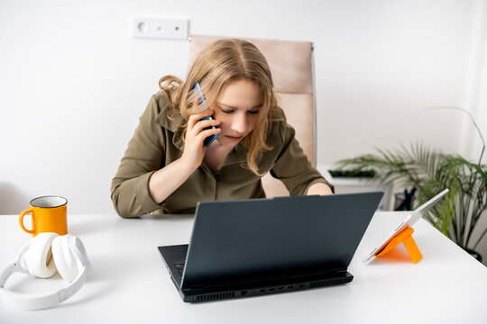 Busy focused woman talking on mobile phone looking at laptop screen in office. Multitasking business communication corporate lifestyle.