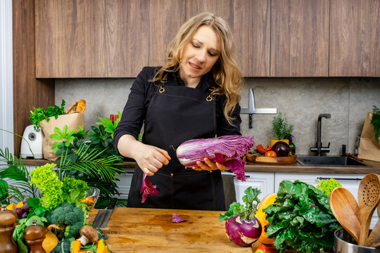 Focused woman culinary expert peeling purple napa cabbage among fresh vegetables kitchen. Healthy organic diet ingredients concept.