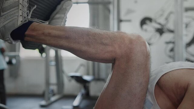 An Indian Asian fit, muscular, confident elderly male or man performs a leg press exercise during a resistance strength training workout in modern gym. Fitness, health, bodybuilding, wellness concept