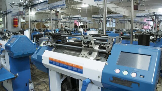 Many automated knitting machines operate inside modern textile factory. Production equipment works across spacious manufacturing hall.