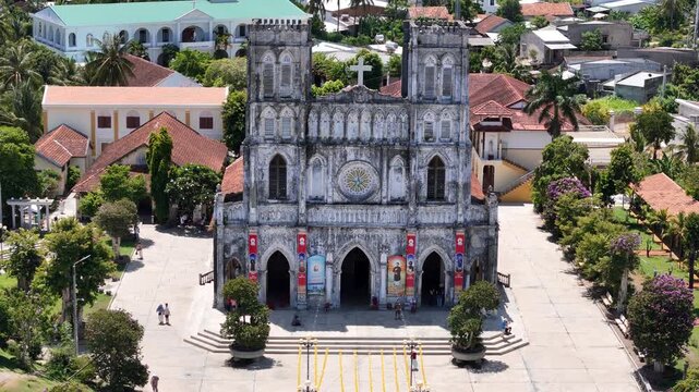 Cinematic drone footage using a 3x telephoto zoom facing the main facade of Mang Lang Church in Phu Yen, Vietnam. The camera gradually pulls backward while tilting upward,