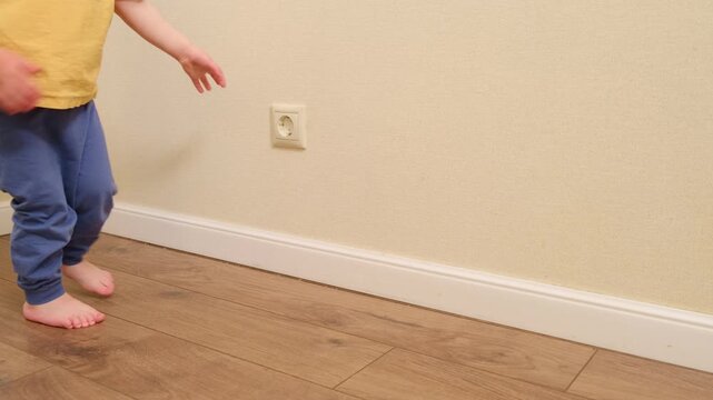 Child touching electrical wall outlet with finger. Dangerous home situation and childhood safety risk. Toddler playing with socket. Prevention of household accident and injury.