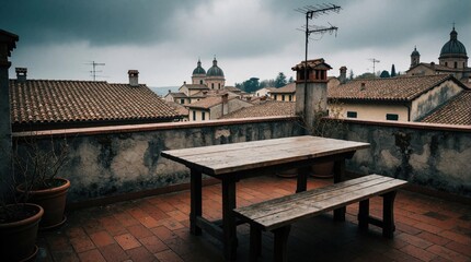 Obraz premium Empty wooden table and bench sit on tiled rooftop overlooking aged Italian town with tiled roofs and domed church. Cloudy sky looms over cityscape.