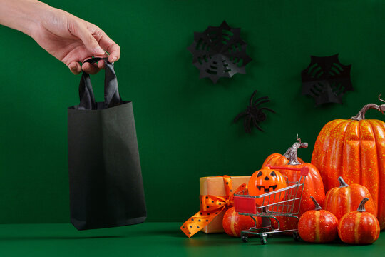Cropped hand holding black shopping bag next to Halloween pumpkins for holiday retail sale
