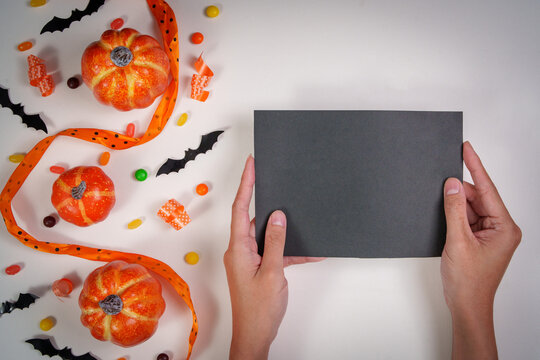 Hands holding blank black card over Halloween background with pumpkins and bats for mockup