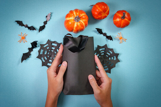 Flat lay of hands holding black paper gift bag for Halloween shopping on blue background