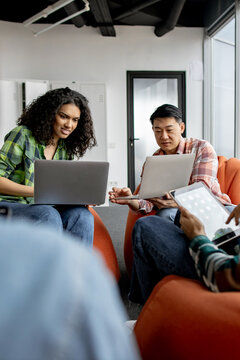 A diverse group of young adults are engaged in a collaborative session, using laptops and tablets in a modern office setting