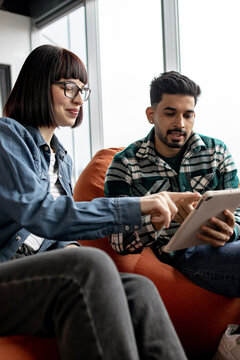 Two young professionals collaborate on a digital project using a tablet device while sitting comfortably in a modern office space