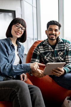 A woman with glasses and a man in a plaid shirt smile while looking at a tablet, suggesting teamwork and modern communication