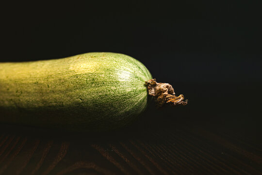 Raw green squash (zucchini) on a table against a dark background; a culinary theme; part of a series.