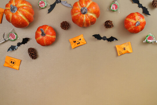 Halloween pumpkins candies and paper bats flat lay on beige background
