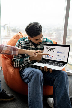 Two colleagues collaborate on a laptop displaying world map and financial charts, discussing business strategy and growth