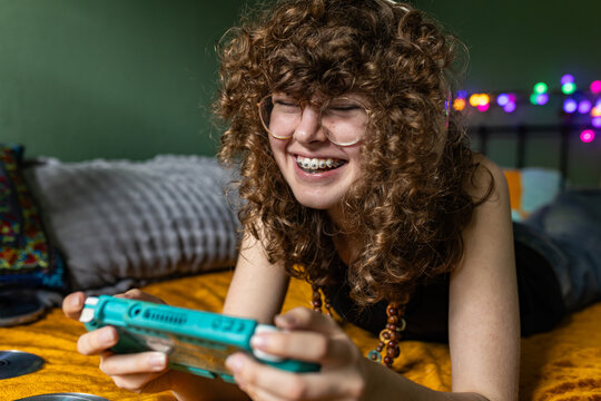 A girl laughs while playing a video game on a bed indoors