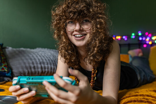 Smiling teenage girl plays video game on bed in her bedroom