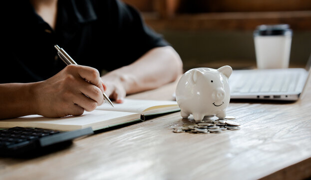 Person putting a coin into a piggy bank while using a calculator, symbolizing saving money, budgeting, financial planning, and personal finance management.