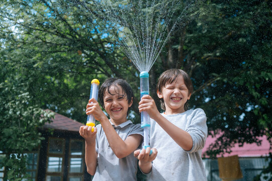 Two happy boys spray water with toys outdoors in the summer garden