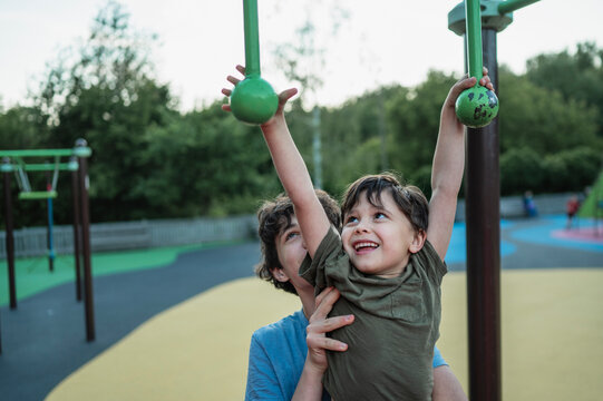 Older brother helps boy on obstacle course at the playground