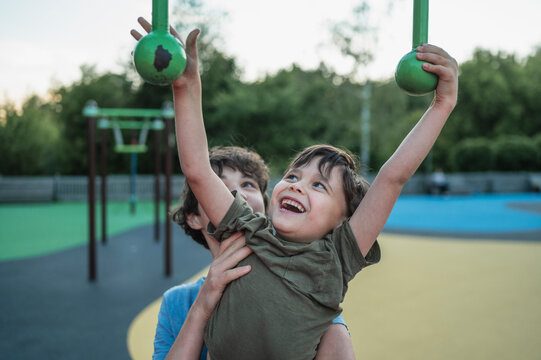 Teenage boy helps brother on outdoor playground obstacle course