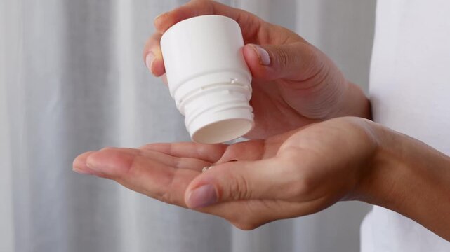 Close up of woman dispensing capsules into palm from white pill bottle for healthcare routine.