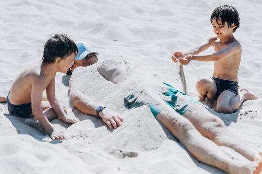 Sons bury their father in the sand at the beach during summer