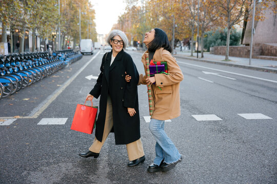 Mother and daughter carry shopping bags across a city street