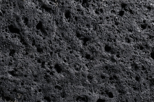 Dark grey porous volcanic lava rock surface texture